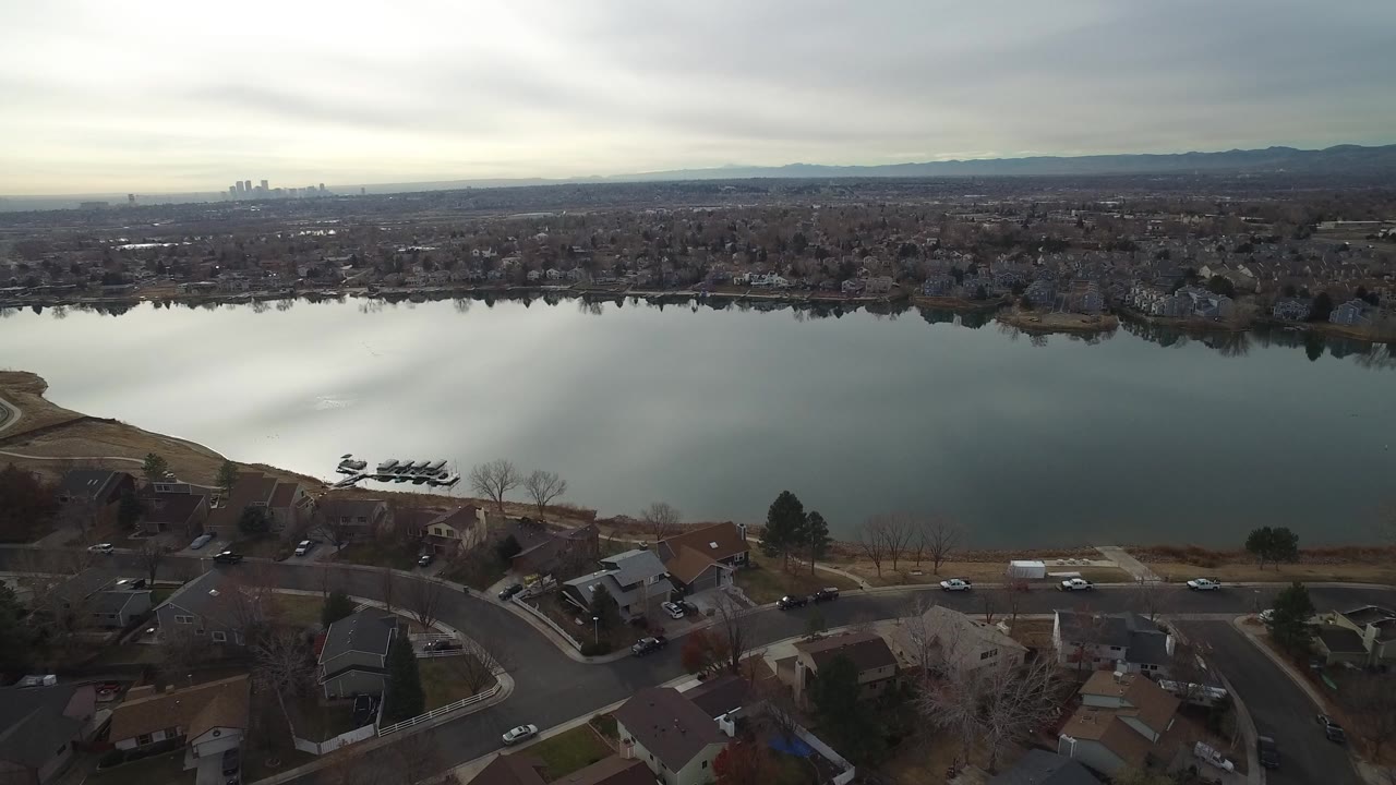 Aerial view over suburban homes and a calm lake under gray sky.