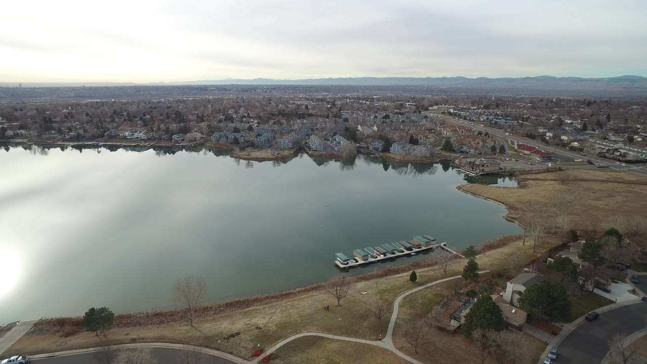 Aerial view over a lake, docks, houses, roads, and distant mountains.