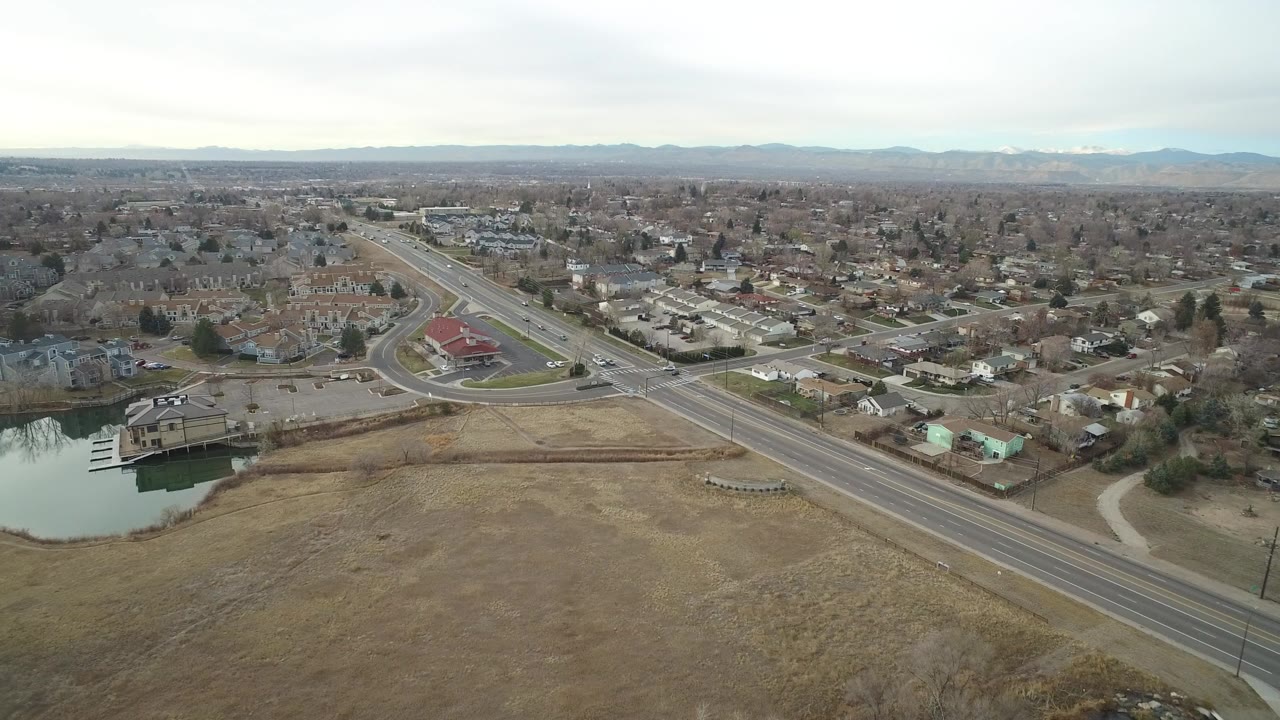 Aerial view of suburban roads, homes, open ground, and distant mountains.