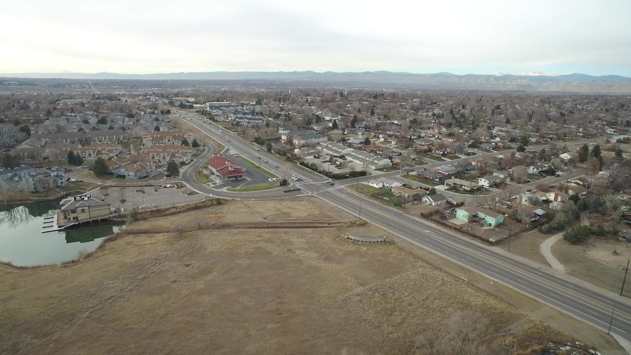 High aerial frame of Westminster, Colorado showing the road intersection slightly closer to center, a pond and docks at lower left, residential blocks, and no visible people.