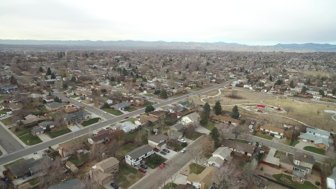 Aerial neighborhood view with houses, roads, lawns, and a park path network.