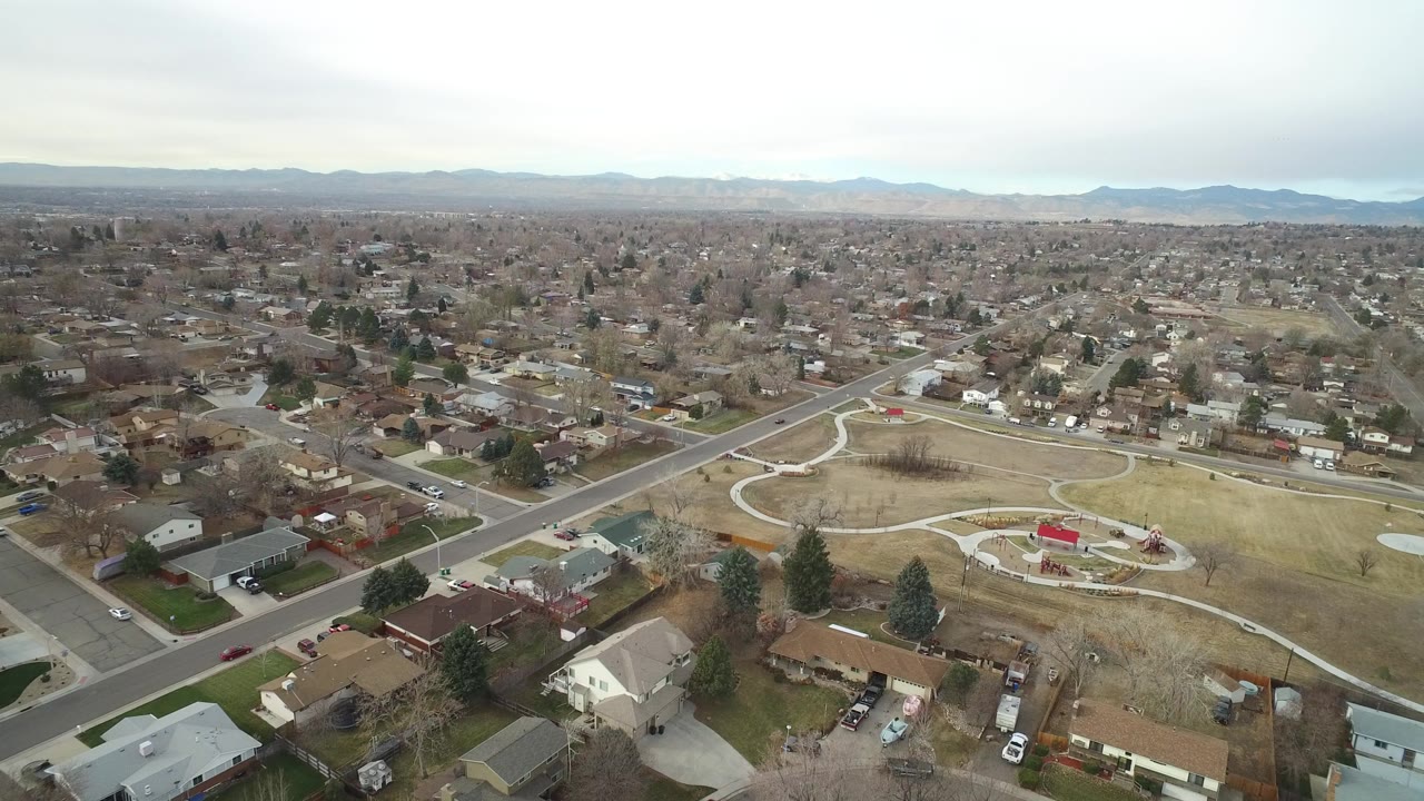 High aerial view of suburban homes, roads, and a park with curving paths.