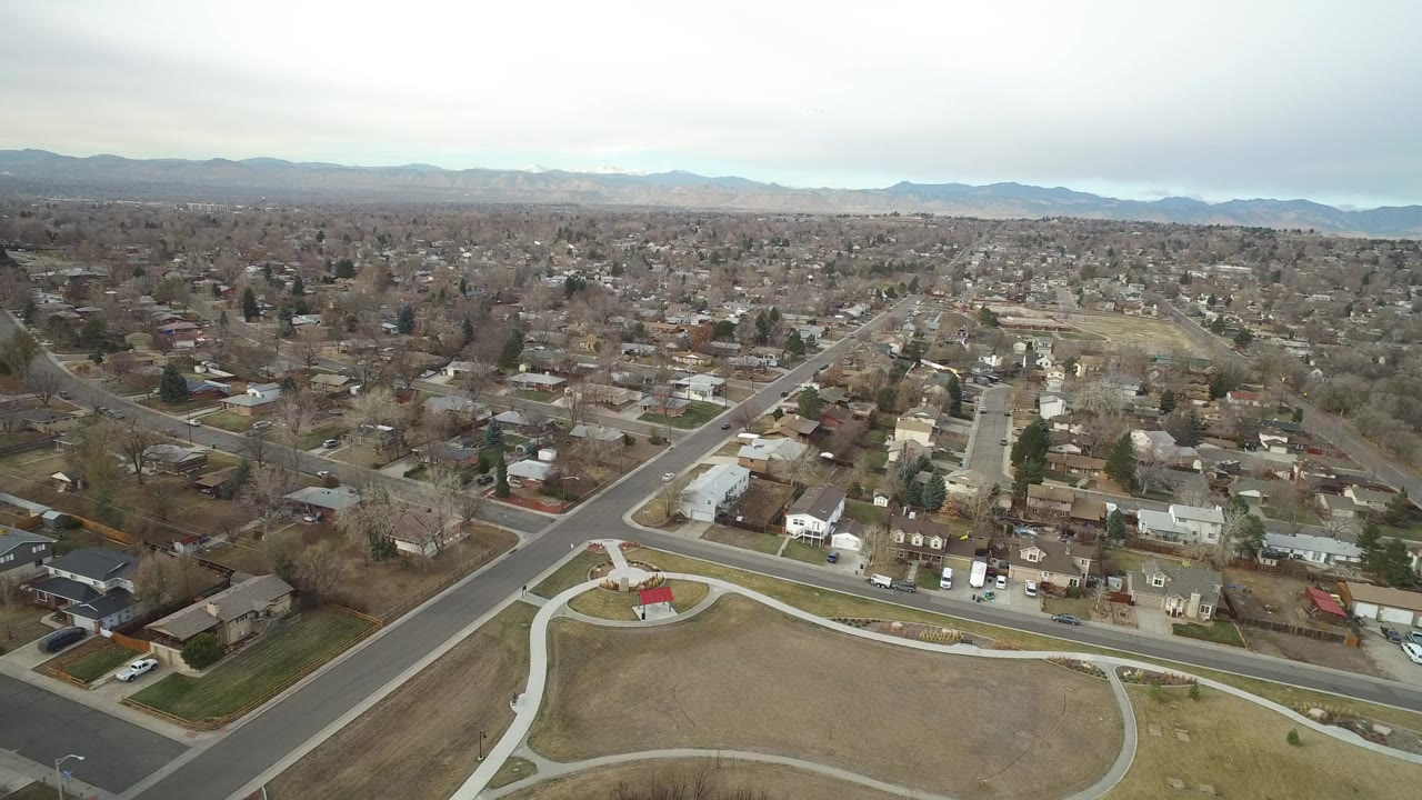 Aerial view of suburban streets, houses, park paths, and distant mountains.