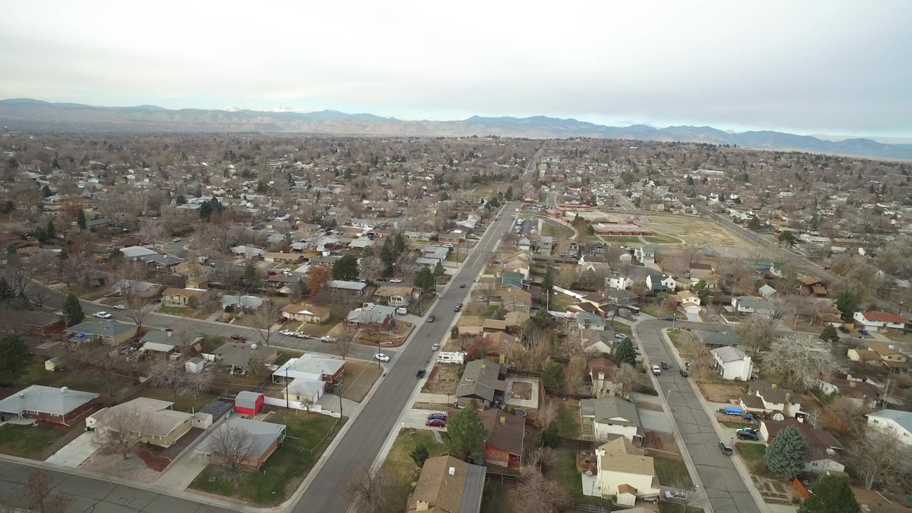 Elevated Westminster, Colorado view centered on a long residential road, surrounding rooftops, leafless trees, distant mountains, and no visible people.
