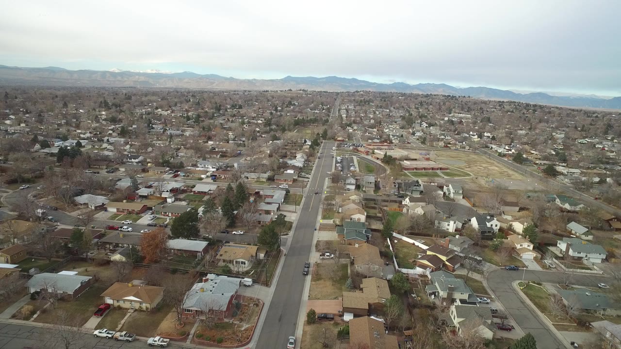Aerial view over suburban homes and a straight road under cloudy sky.