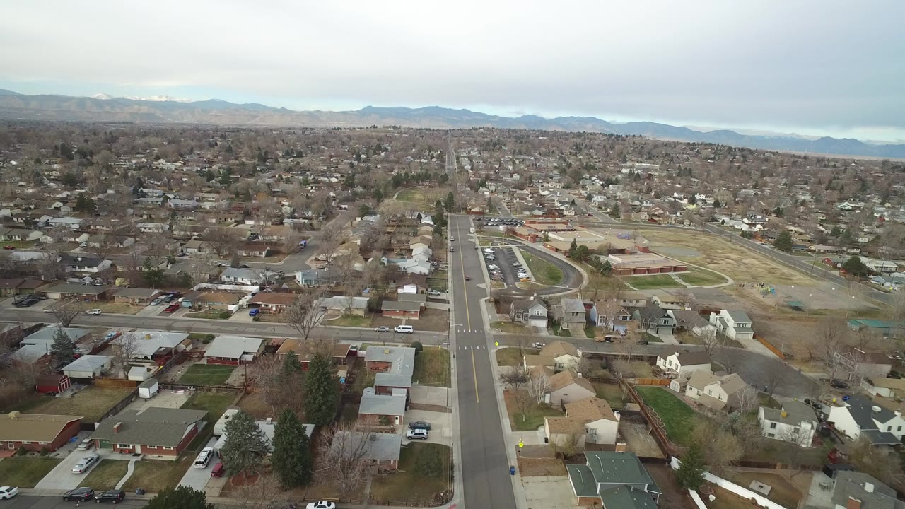 Aerial view over suburban homes, roads, fields, and distant mountains.