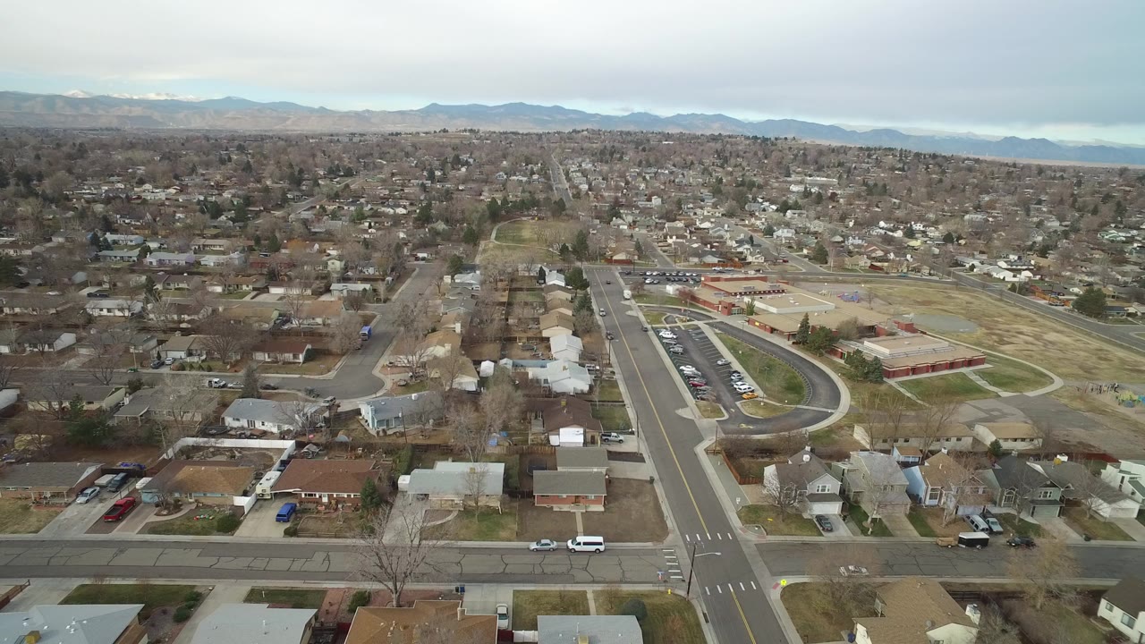 Aerial view over suburban streets, houses, a campus area, and distant mountains.