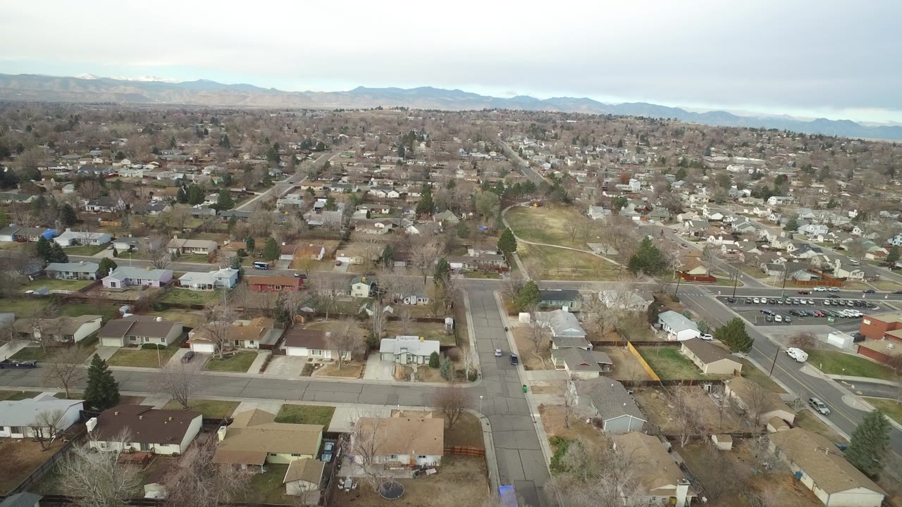 Wide aerial of homes, intersecting roads, cars, and a small green area.