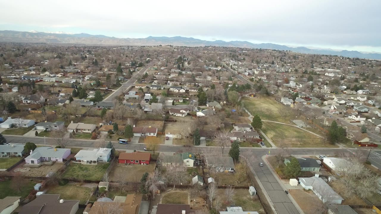 Aerial view over suburban homes and streets with distant hills.
