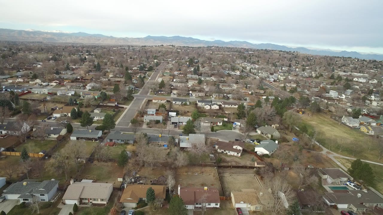 Aerial view over suburban houses and streets with distant mountains.