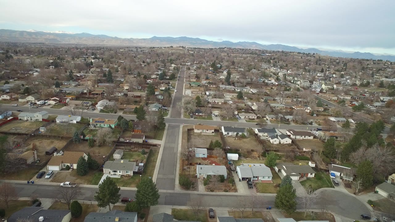 Aerial view over suburban homes and straight roads under a pale sky.