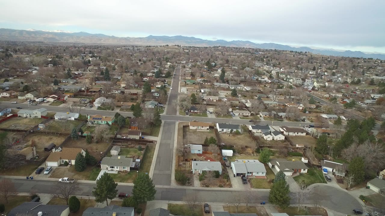 Early aerial frame over Westminster, Colorado showing a long straight neighborhood road, clustered houses, bare trees, and no visible people.