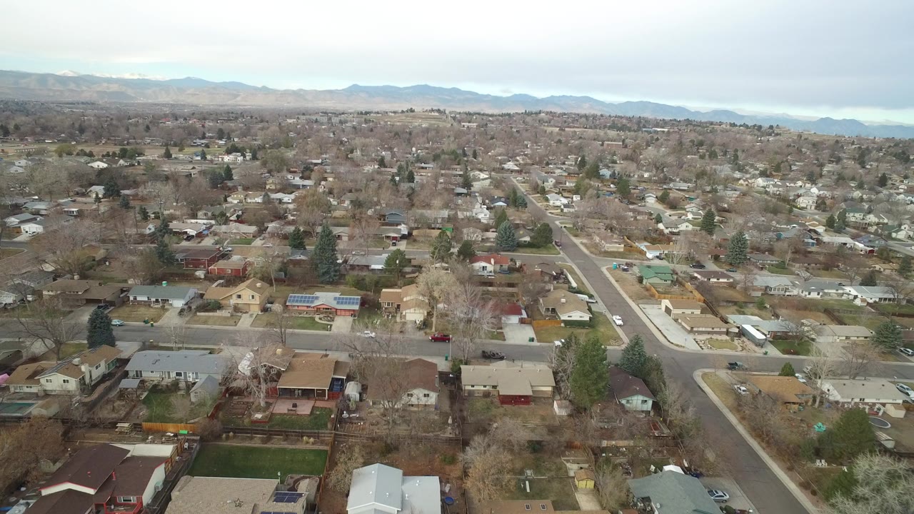 High aerial view over a suburban neighborhood with houses and distant mountains.