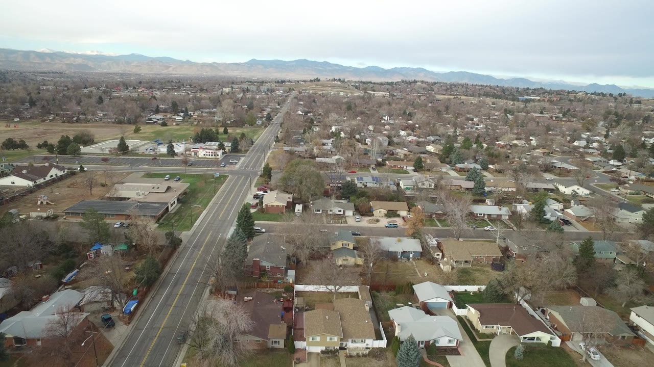 Suburban aerial view with a wide roadway, homes, businesses, and mountains in the distance.