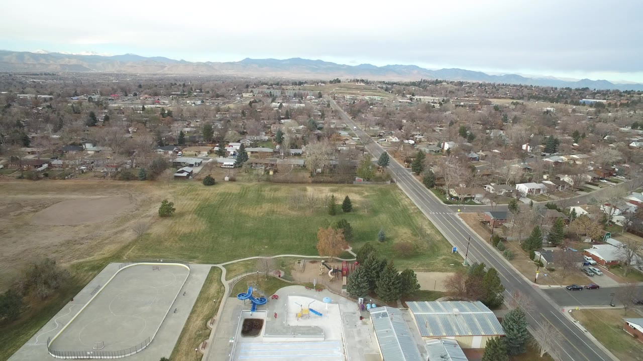 Aerial view of a park, road, houses, and distant mountains.