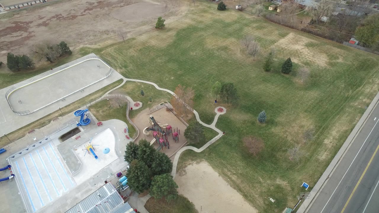 Overhead drone view of lawns, paths, playground, pool area, and road.