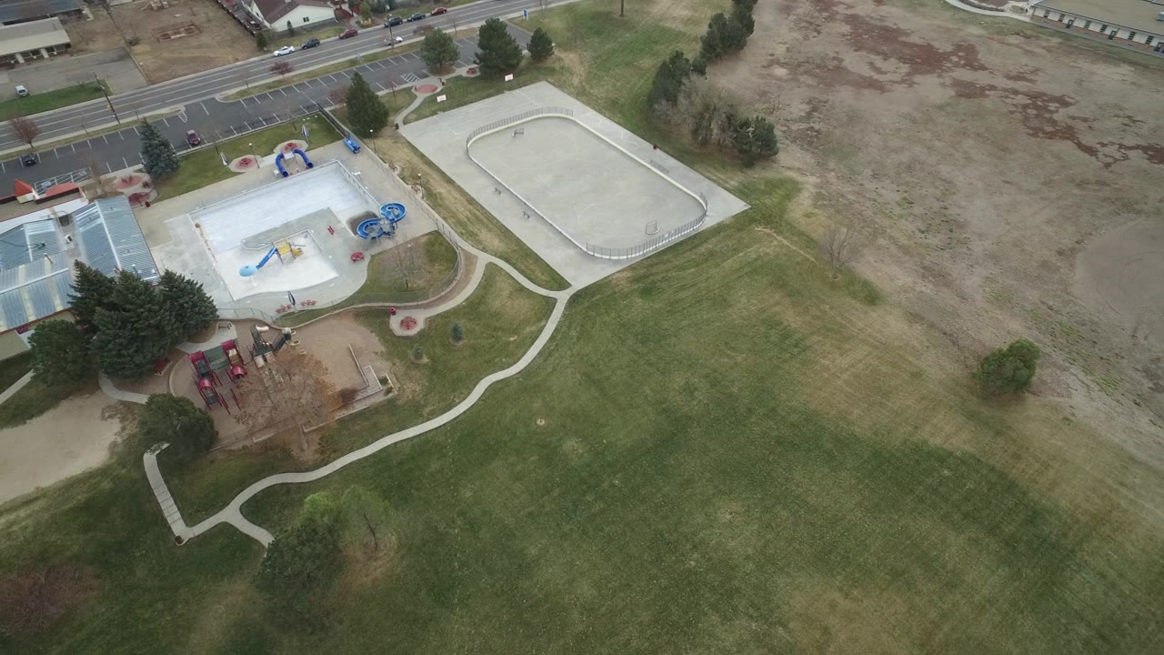 Overhead park view with grass, playground, paths, and road edges.