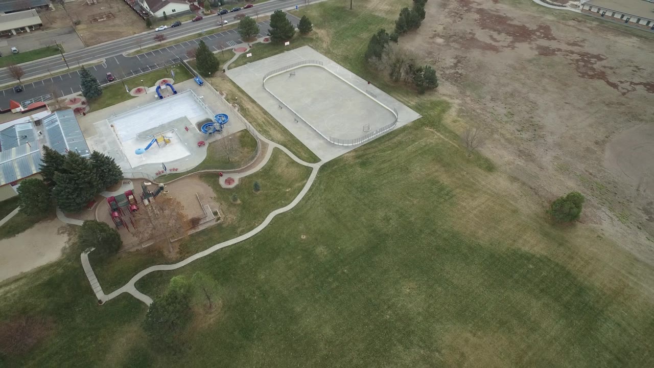 Top-down Westminster, Colorado frame showing the playground and pale recreational surface near the upper left, an oval paved area to the right, broad lawn below, and no visible people.