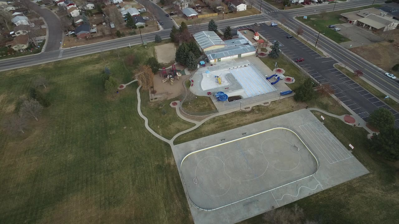 Aerial view of a park, sport court, building, parking lot, roads, and houses.