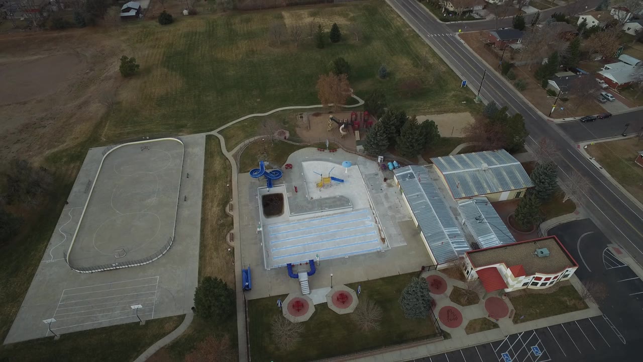 Aerial view of a building, empty paved lot, playground, lawns, and residential streets.