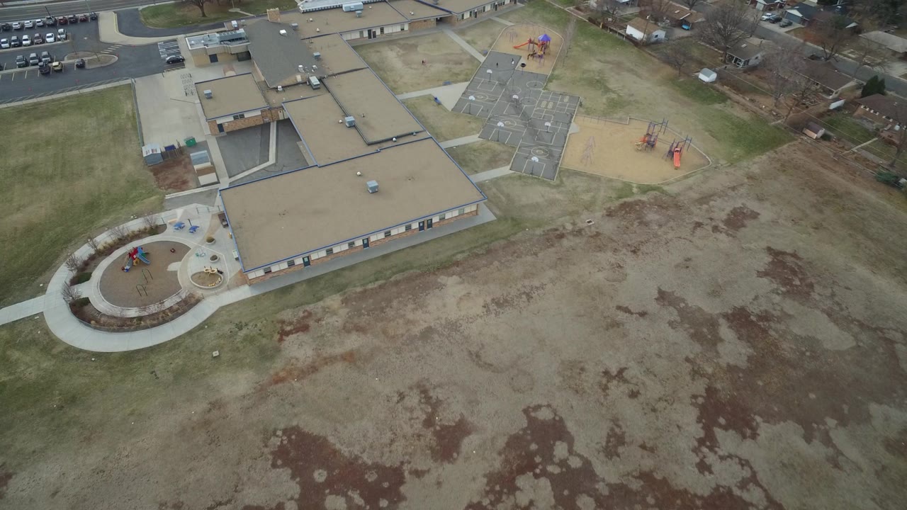 Drone view over a suburban building, sidewalks, playgrounds, and open grass.