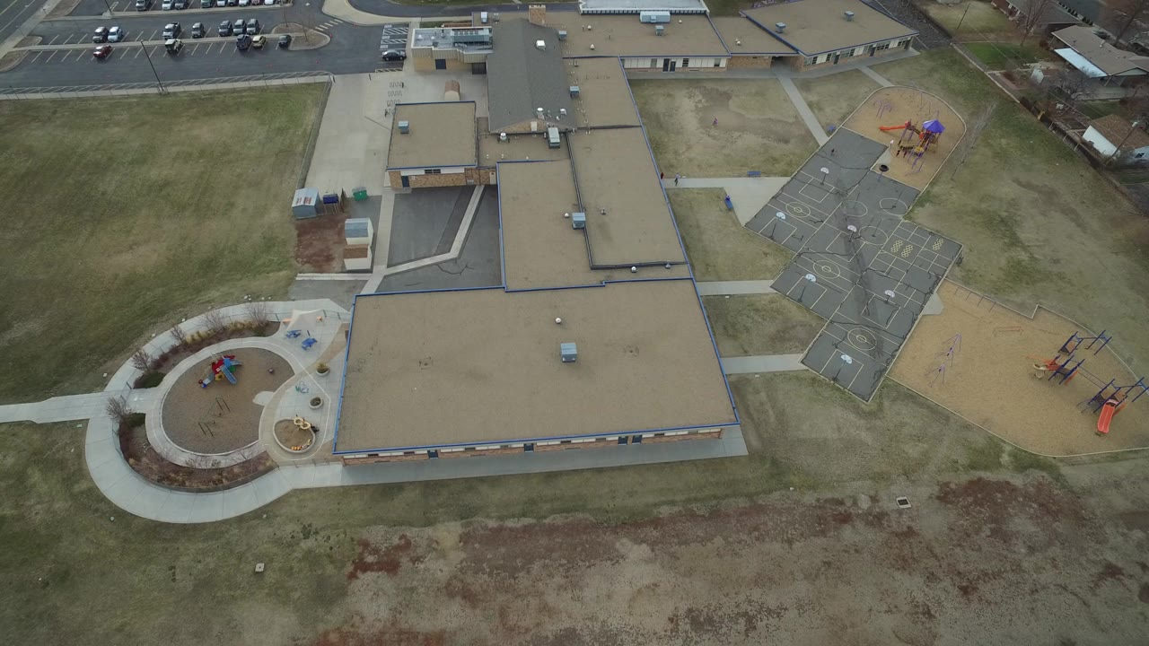 Overhead view of a flat-roofed building with grass, sidewalks, playgrounds, and parking.