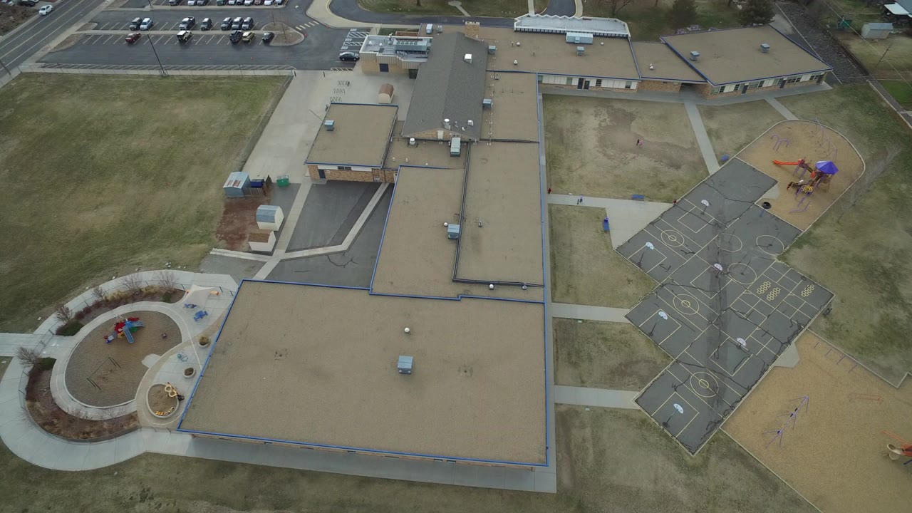 Overhead view of flat-roofed buildings, play areas, lawns, and roads.