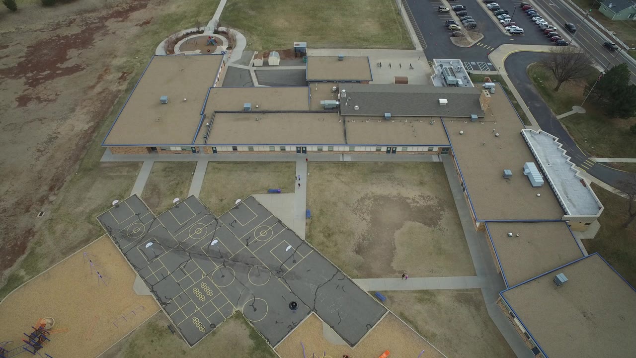 Aerial view of a school roof, playground courts, sidewalks, grass, and parking area.