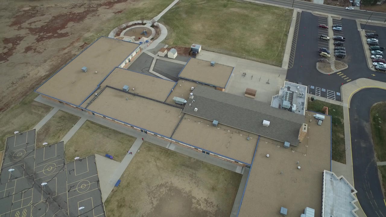 Steep aerial view of a building complex beside a road, parking area, and courts.