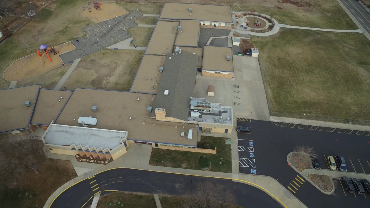 Overhead view of a low-rise building, parking lot, sidewalks, and playground area.