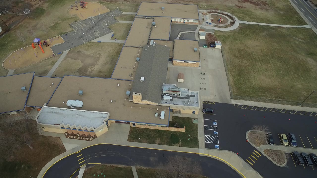 Second overhead frame in Westminster, Colorado showing the office building roofs centered over drive lanes, empty parking stalls, small parked cars, lawn, and no visible people.
