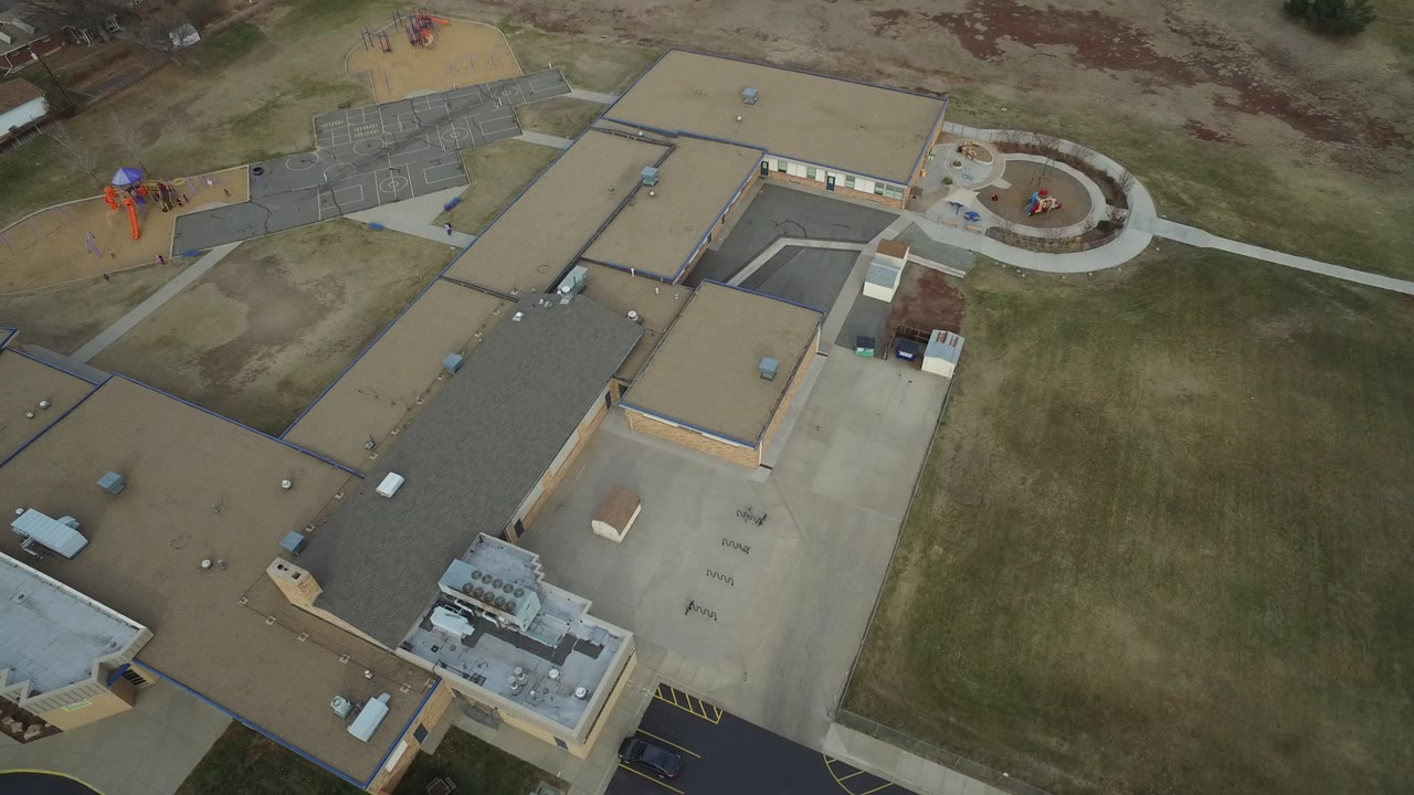 High aerial view of a school building, playground, fields, and paths.