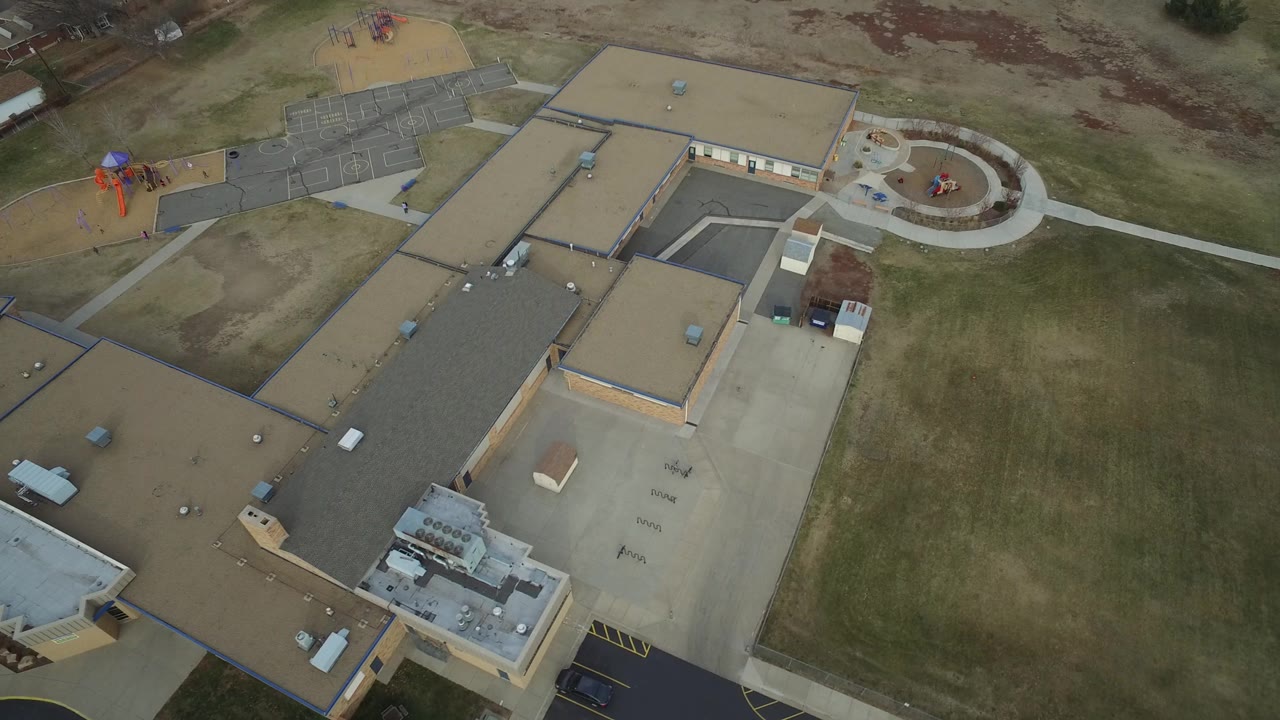 Drone-height view of the Westminster school campus with tan roofs, a circular entrance plaza to the right, playground equipment to the upper left, and no visible people.