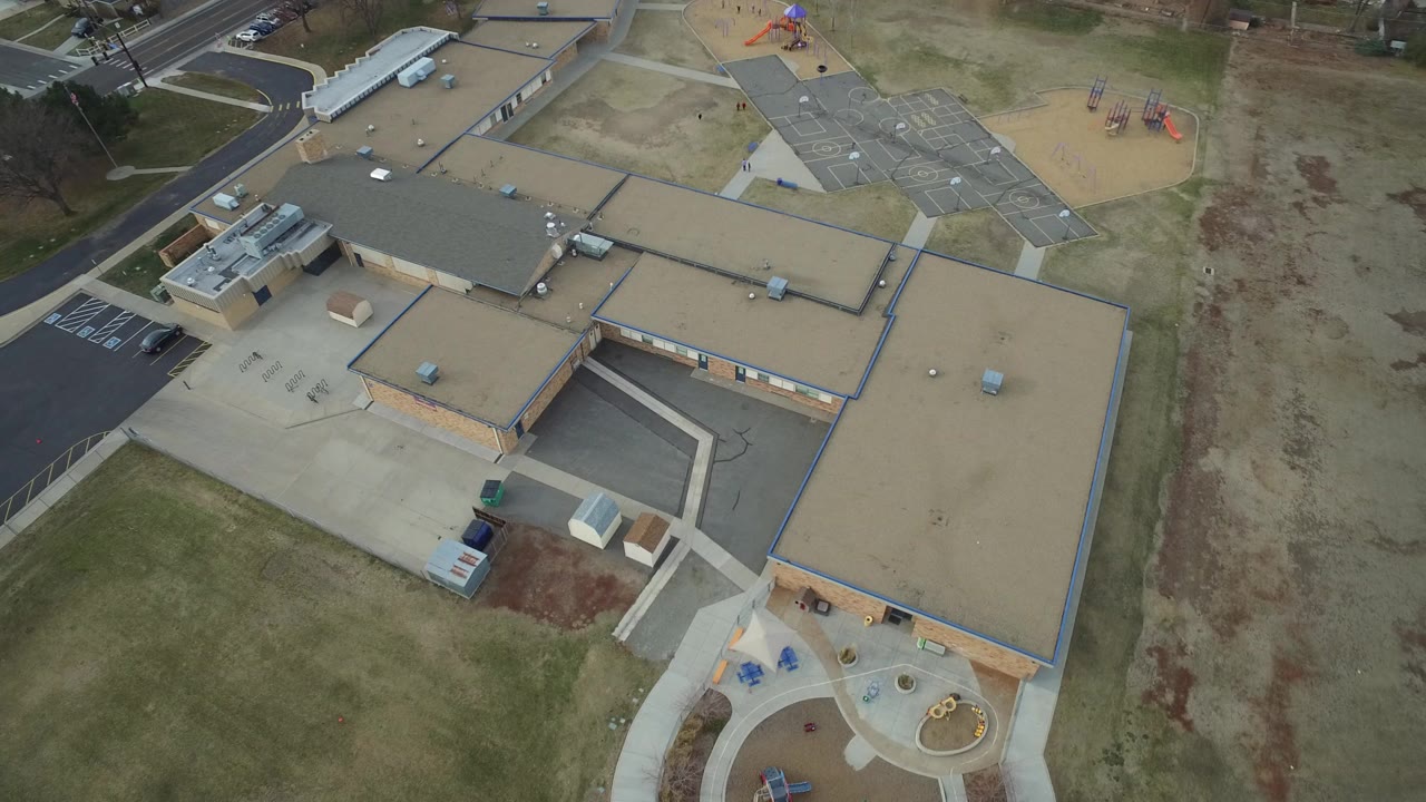 Overhead view of a school roof, courtyard paths, playground, lawns, and parking areas.