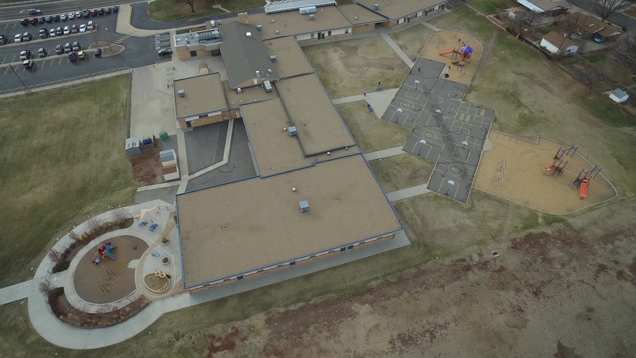 Aerial view of a tan-roofed building with playgrounds and sidewalks.