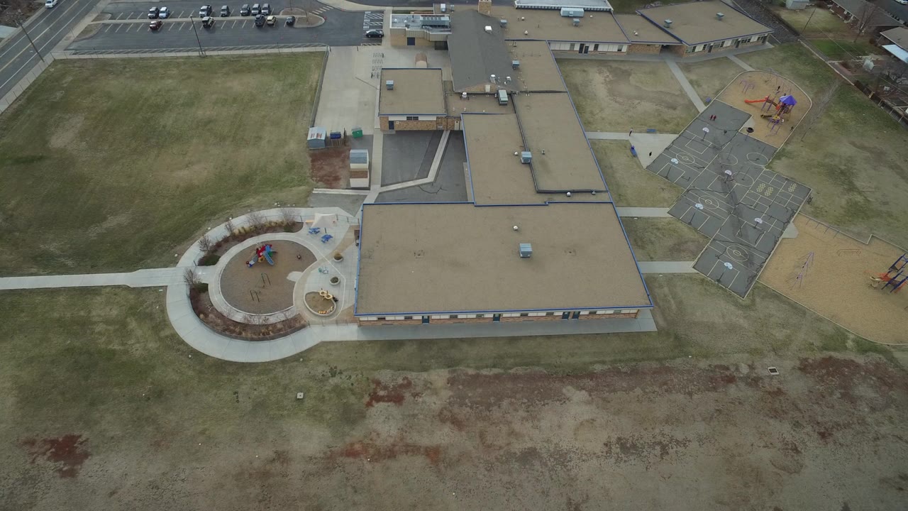 Overhead view of a low-rise building, playground, road, and open grass.