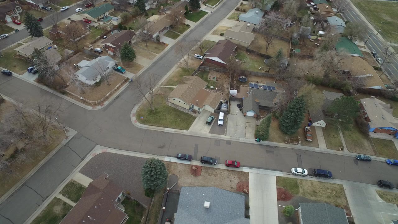 Aerial view of a suburban intersection with houses, yards, cars, and bare trees.