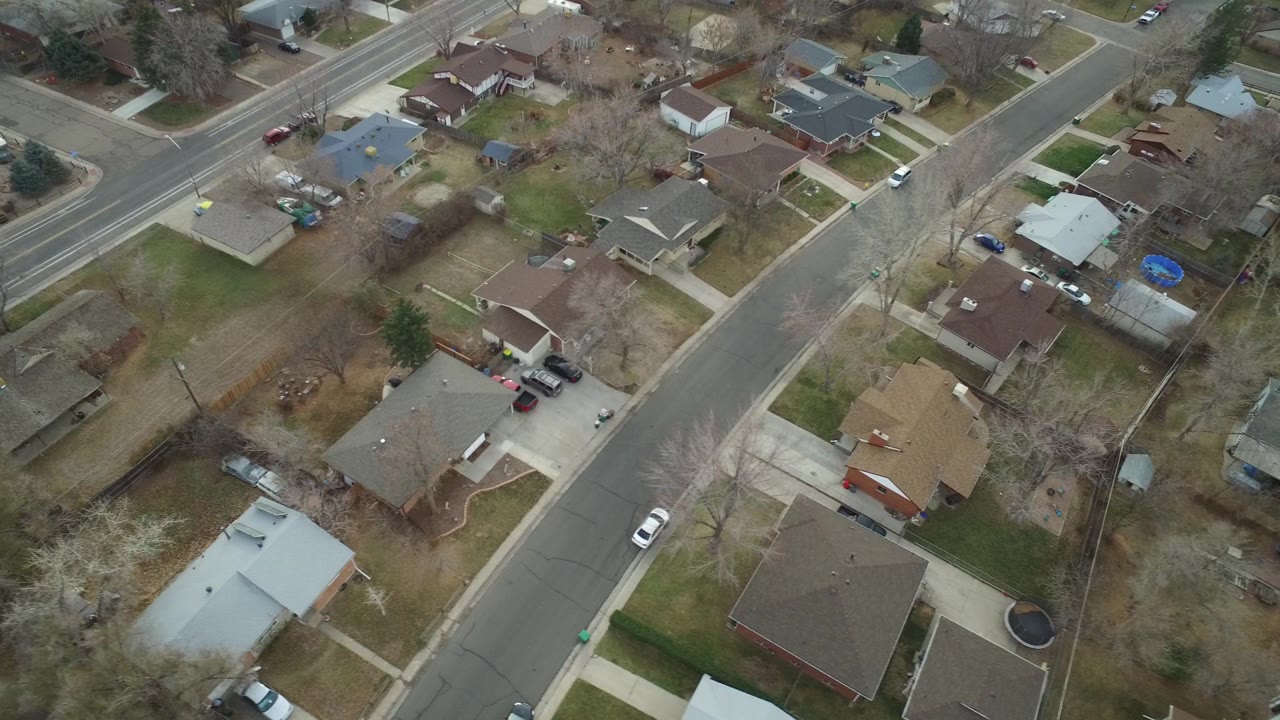 Elevated Westminster, Colorado view showing rooftops, backyards, driveways, parked cars, and a larger road beyond the neighborhood, with no visible people.
