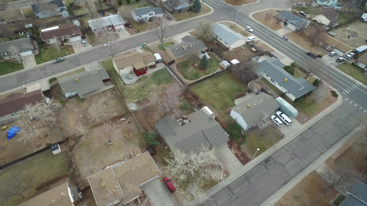 Aerial view over Westminster, Colorado residential blocks with rooftops, bare yards, a cross street, and several parked vehicles, with no clearly visible people.