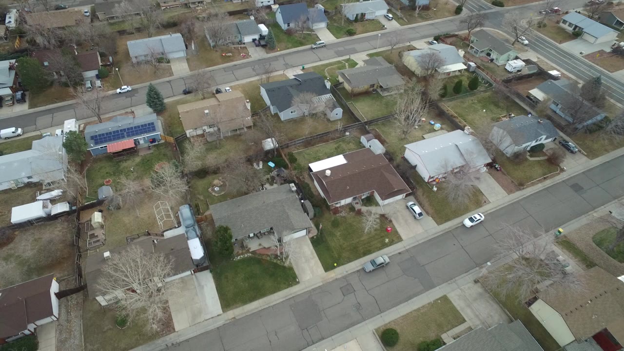Overhead drone view of a Westminster, Colorado residential block with single-family homes, leafless trees, driveways, and parked cars, with no visible people.