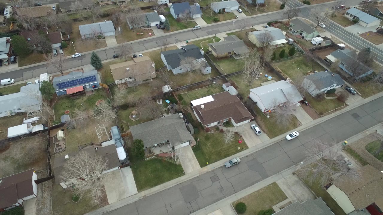 Aerial view over Westminster, Colorado homes where a rooftop solar array, fenced yards, driveways, and residential streets are visible, with no visible people.