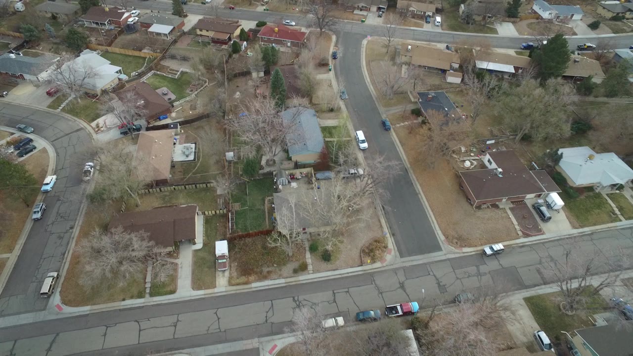 Aerial Westminster, Colorado view centered on a curved neighborhood intersection with rooftops, fenced yards, driveways, bare trees, and no visible people.