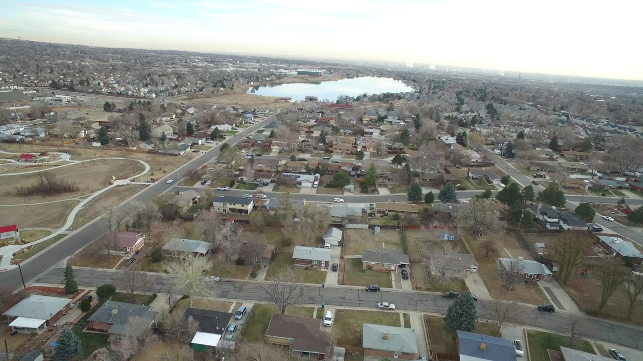 Aerial view over suburban homes, roads, and a distant lake