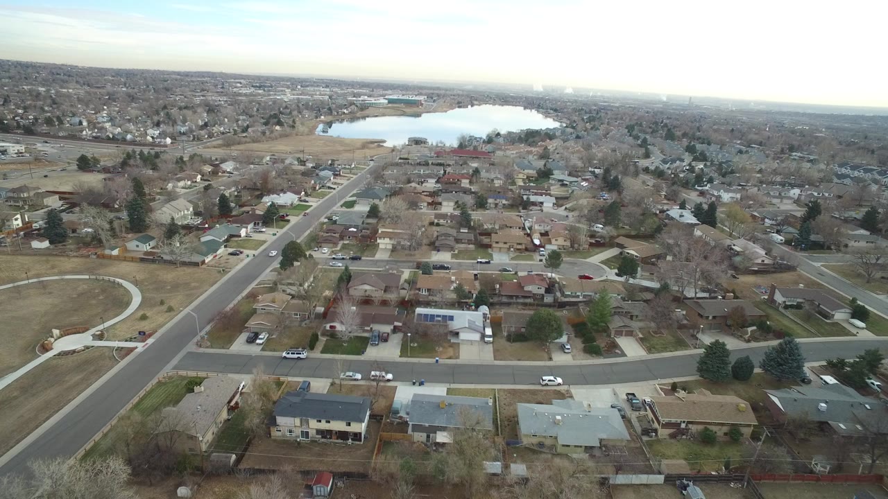 Aerial view of suburban homes, roads, and a lake beyond the neighborhood.
