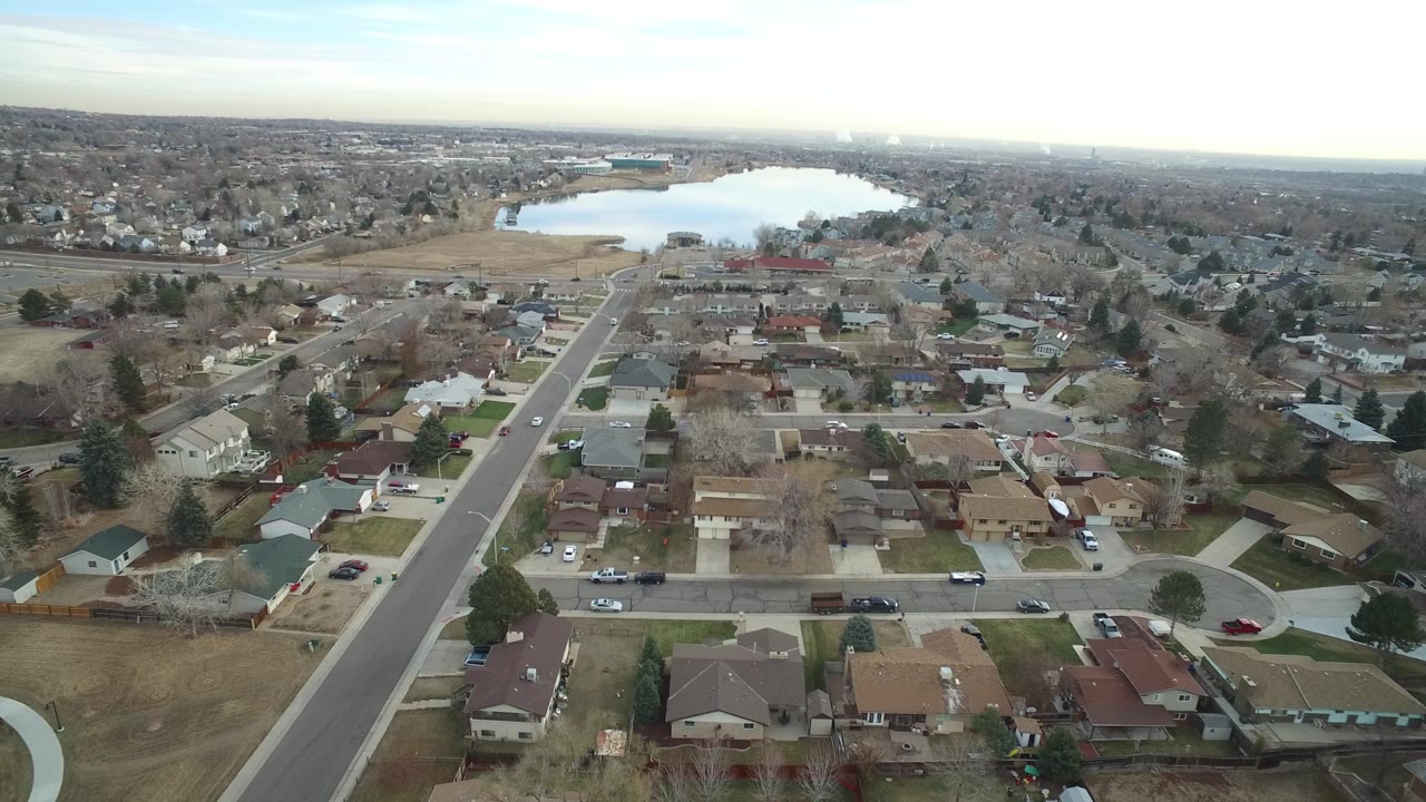 Opening aerial view over Westminster, Colorado homes and a straight residential street leading toward a lake, with no visible people.