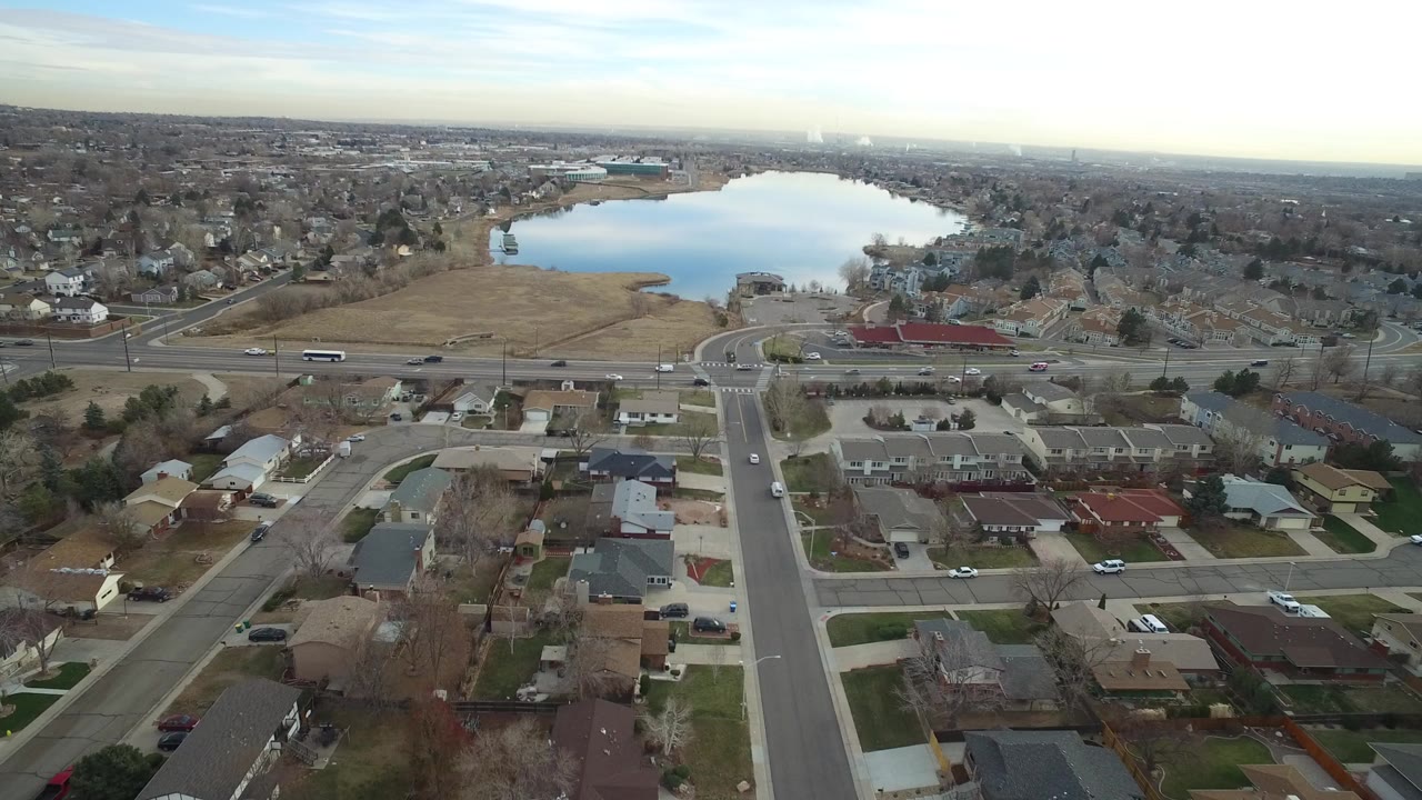 Aerial view of suburban streets, homes, traffic, and a lake beyond.