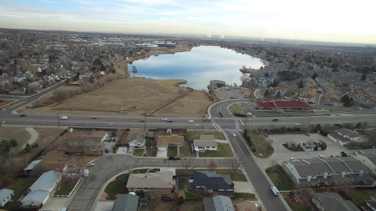 Aerial view of a suburban road, homes, fields, and a lake.