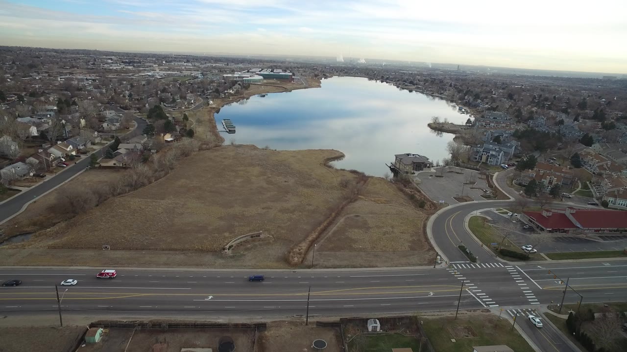 Aerial view of a suburban road, open field, homes, and lake.