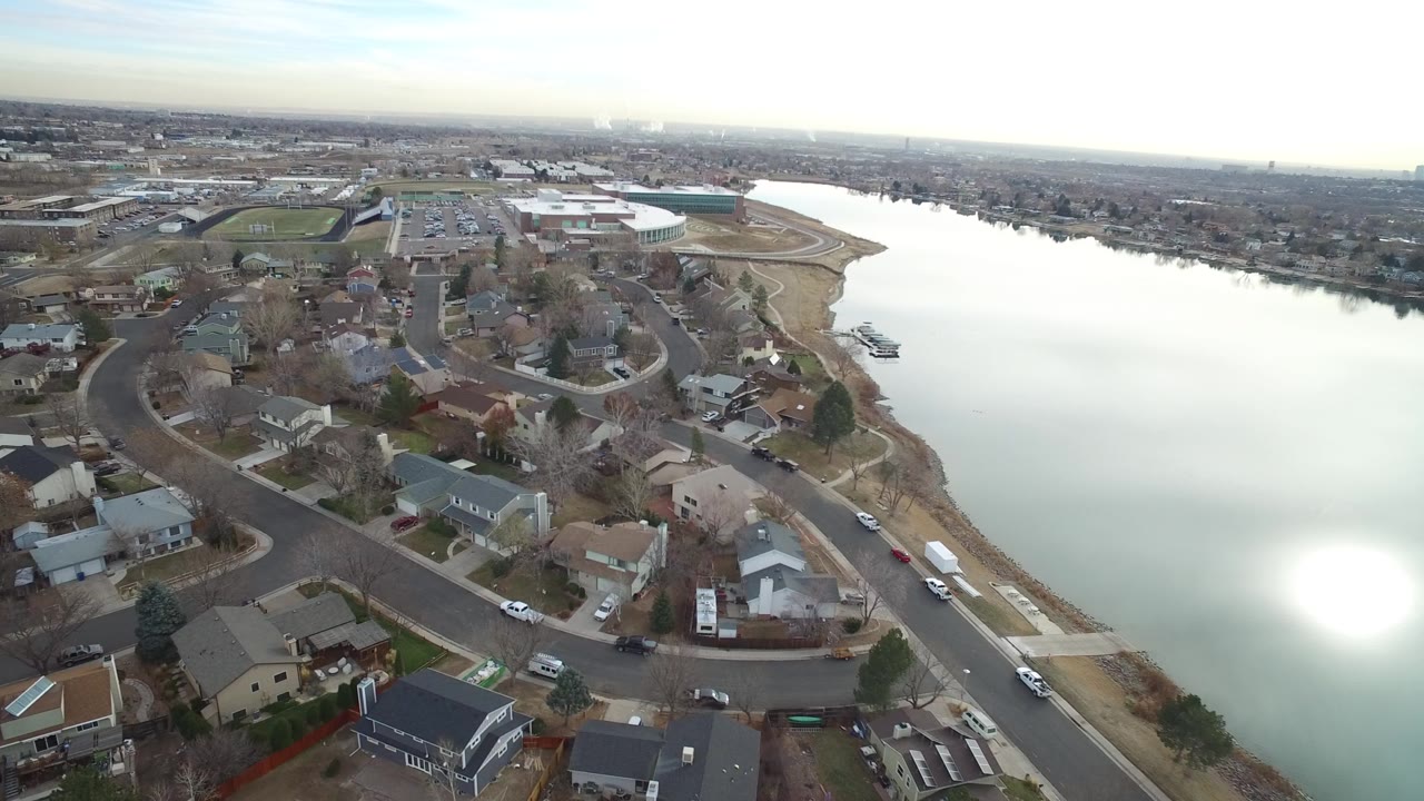 Aerial view over Westminster, Colorado homes and curving streets beside a wide river, with bright sun reflection on the water and no visible people.