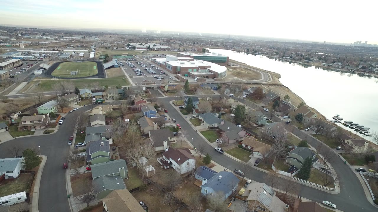 Aerial view of suburban homes beside a lake and school athletic fields.